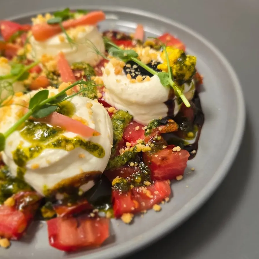 Burrata crémeuse, tomates du pays, pesto de basilic et crumble croustillant, dressée à L'Entre Deux.