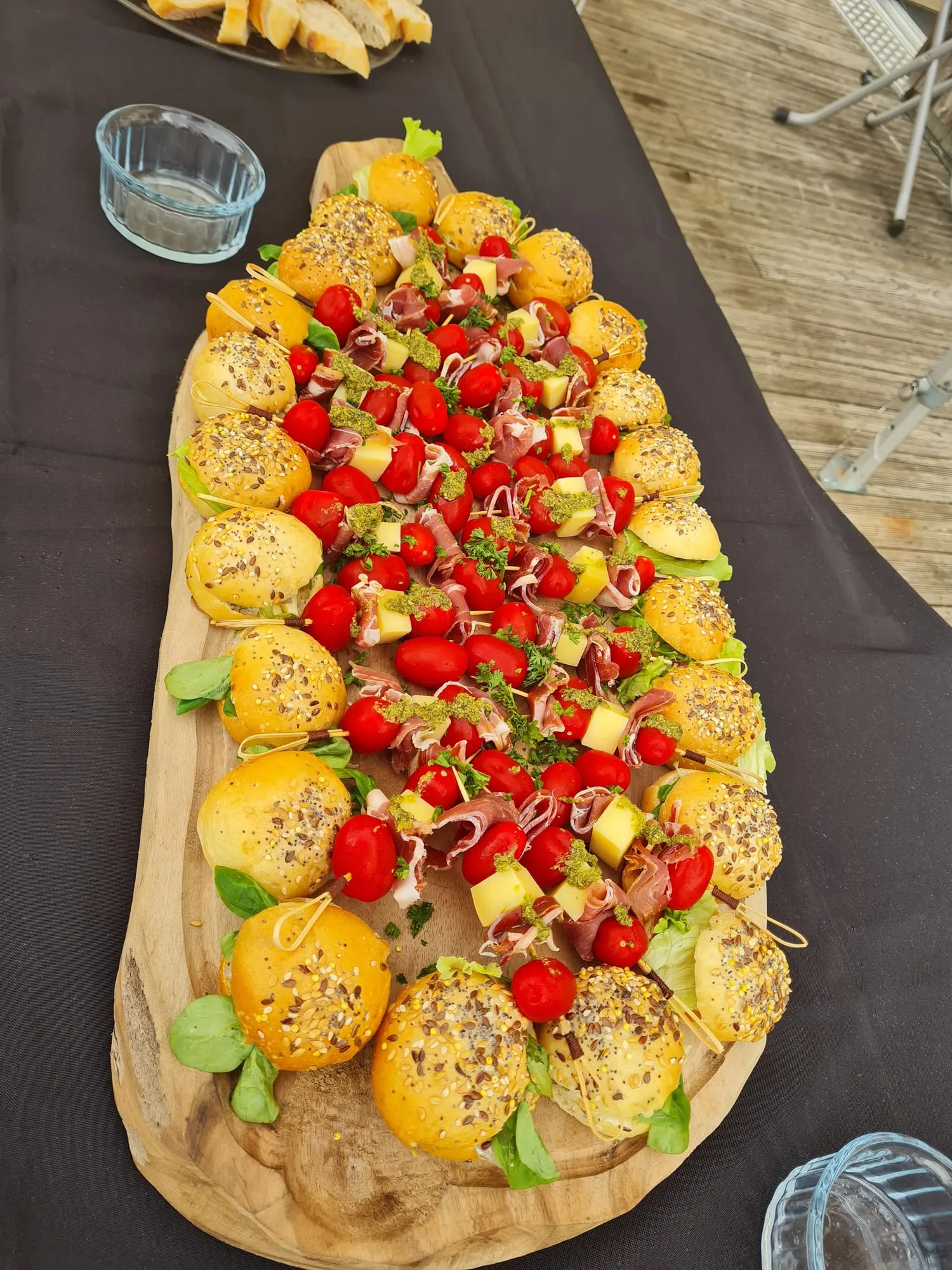 Planche en bois garnie de mini burgers et de brochettes de tomates cerises.