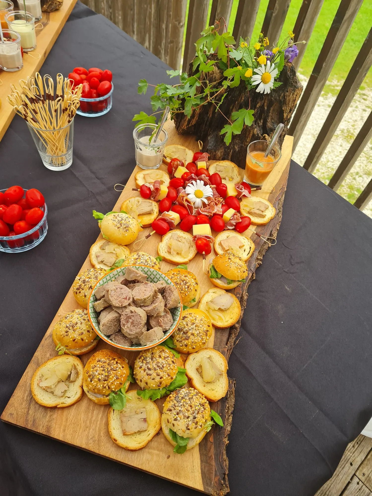 Planche de petits pains garnis et de brochettes, décorée de fleurs des champs.